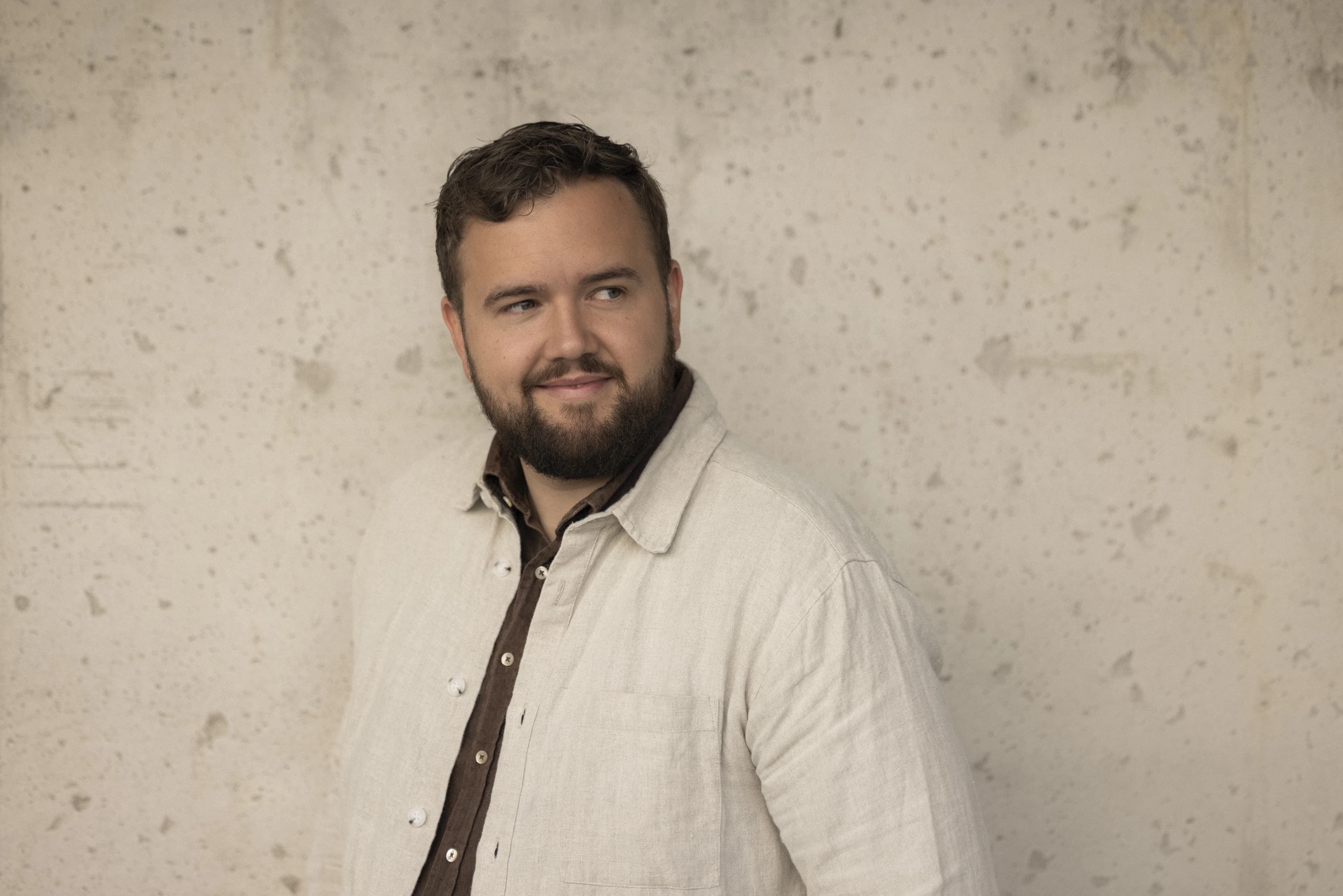 Portrait of a smiling bearded man against a light wall.