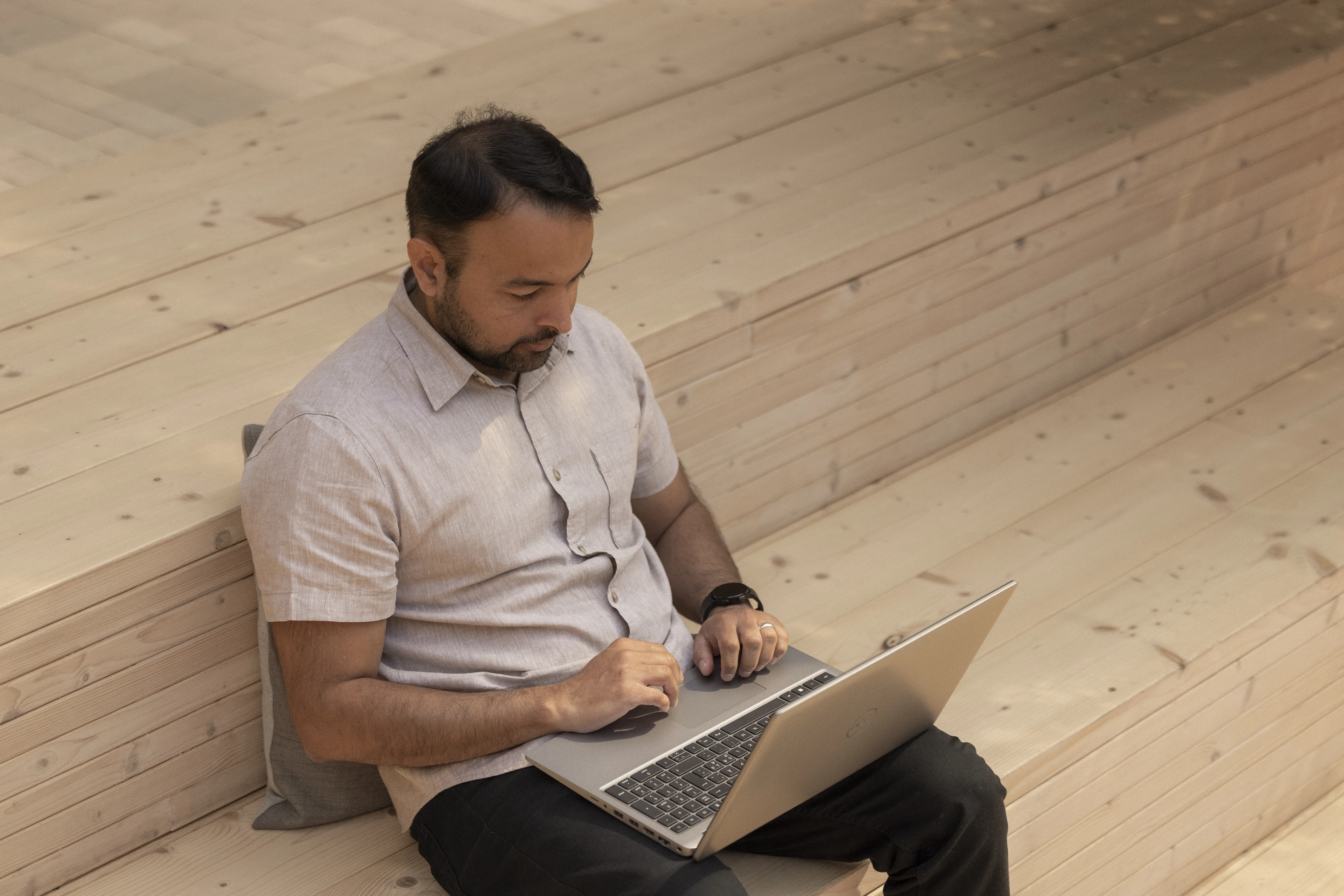 Mann arbeitet mit Laptop auf einer Holztreppe.