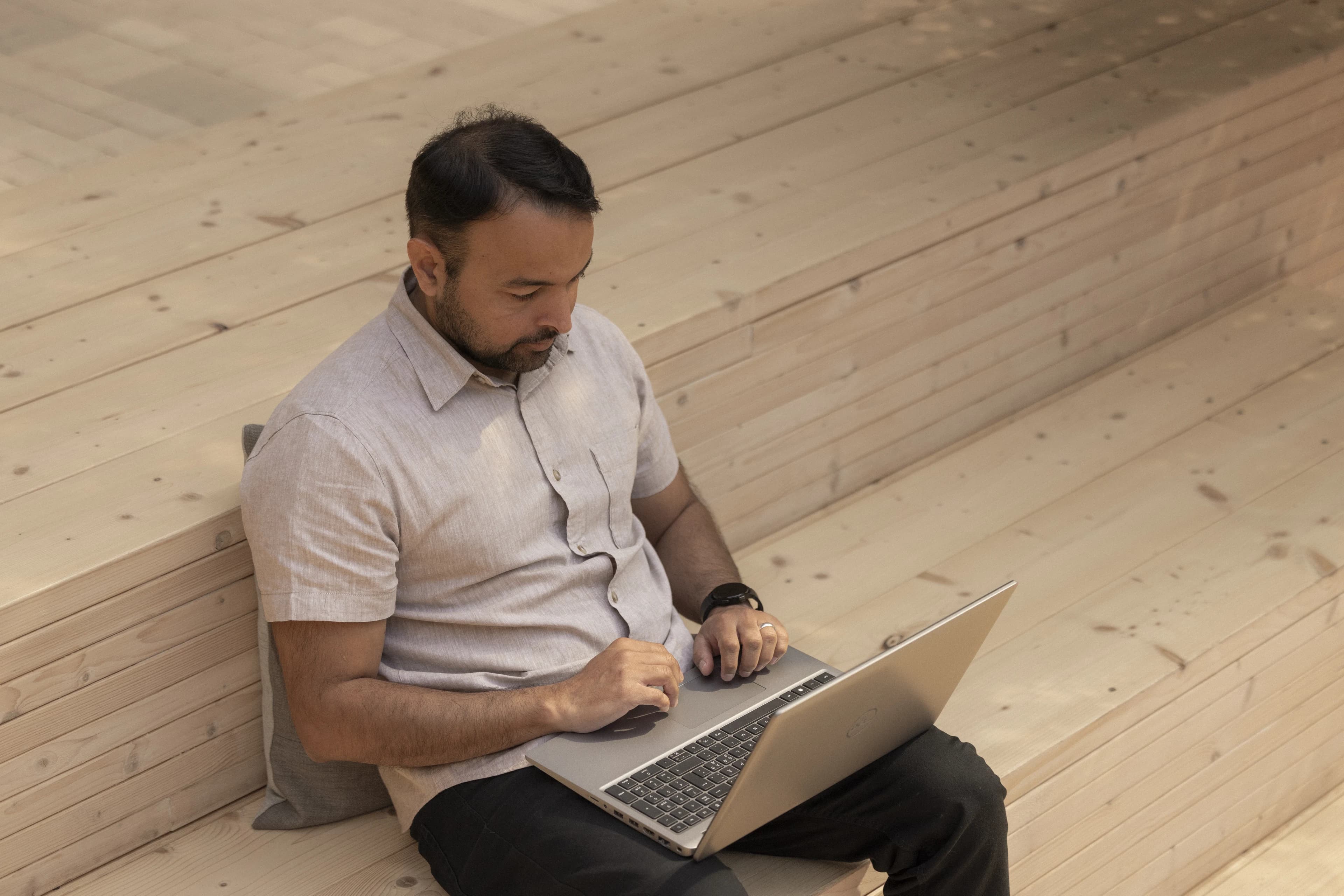 Man working on a laptop on a wooden staircase.