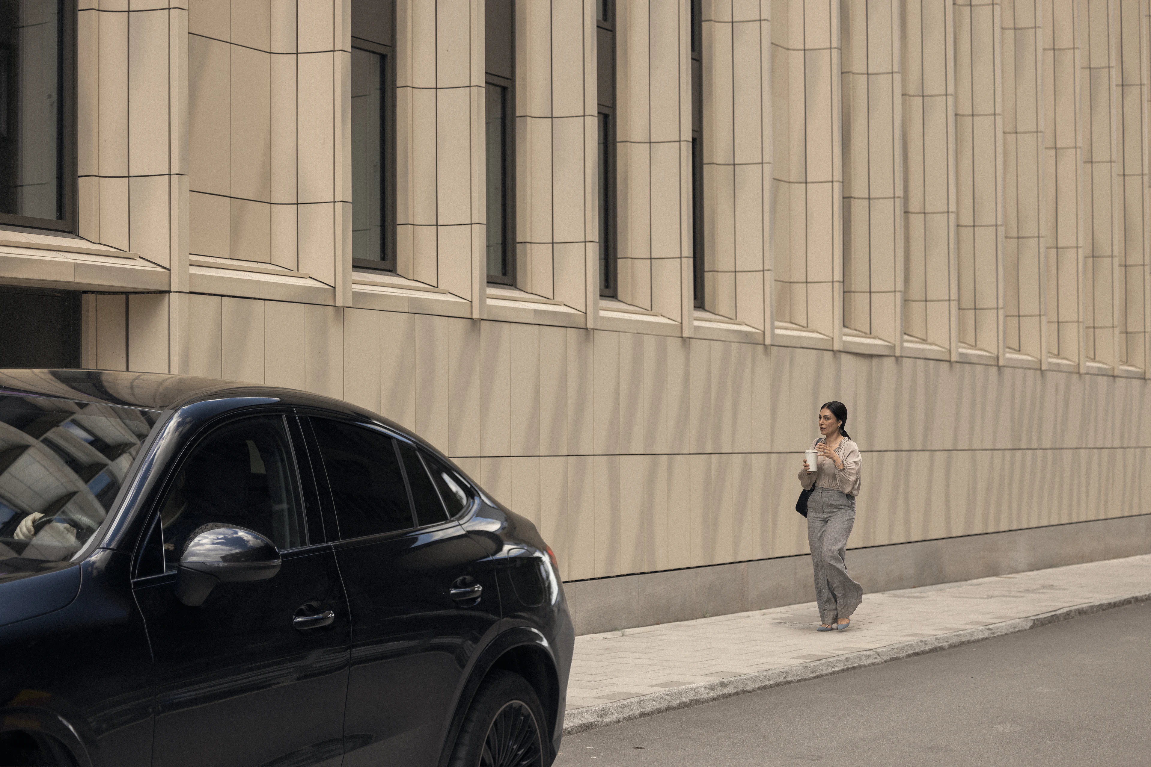 Dunkles Auto vor einem Gebäude, im Hintergrund eine Person.